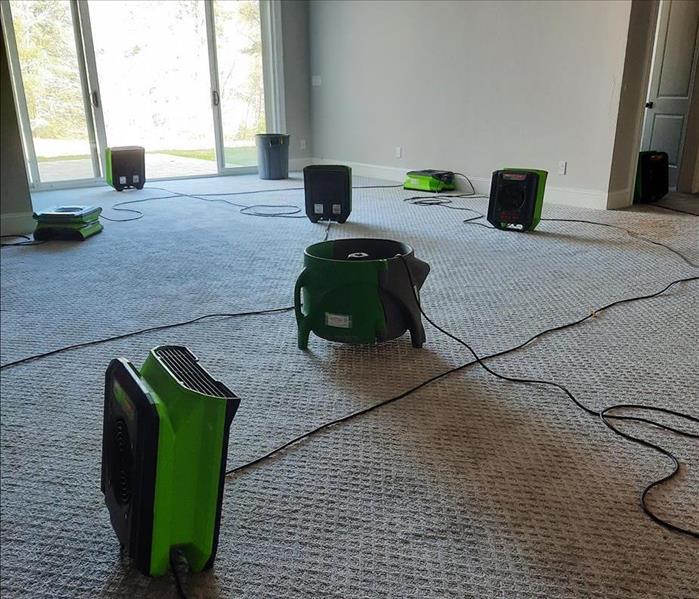 Multiple SERVPRO air movers near a dehumidifier on a carpeted floor near patio doors and damaged ceiling